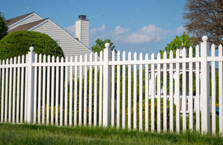 White vinyl fence in a cottage village tall thuja bushes behind the fence fencing of private property